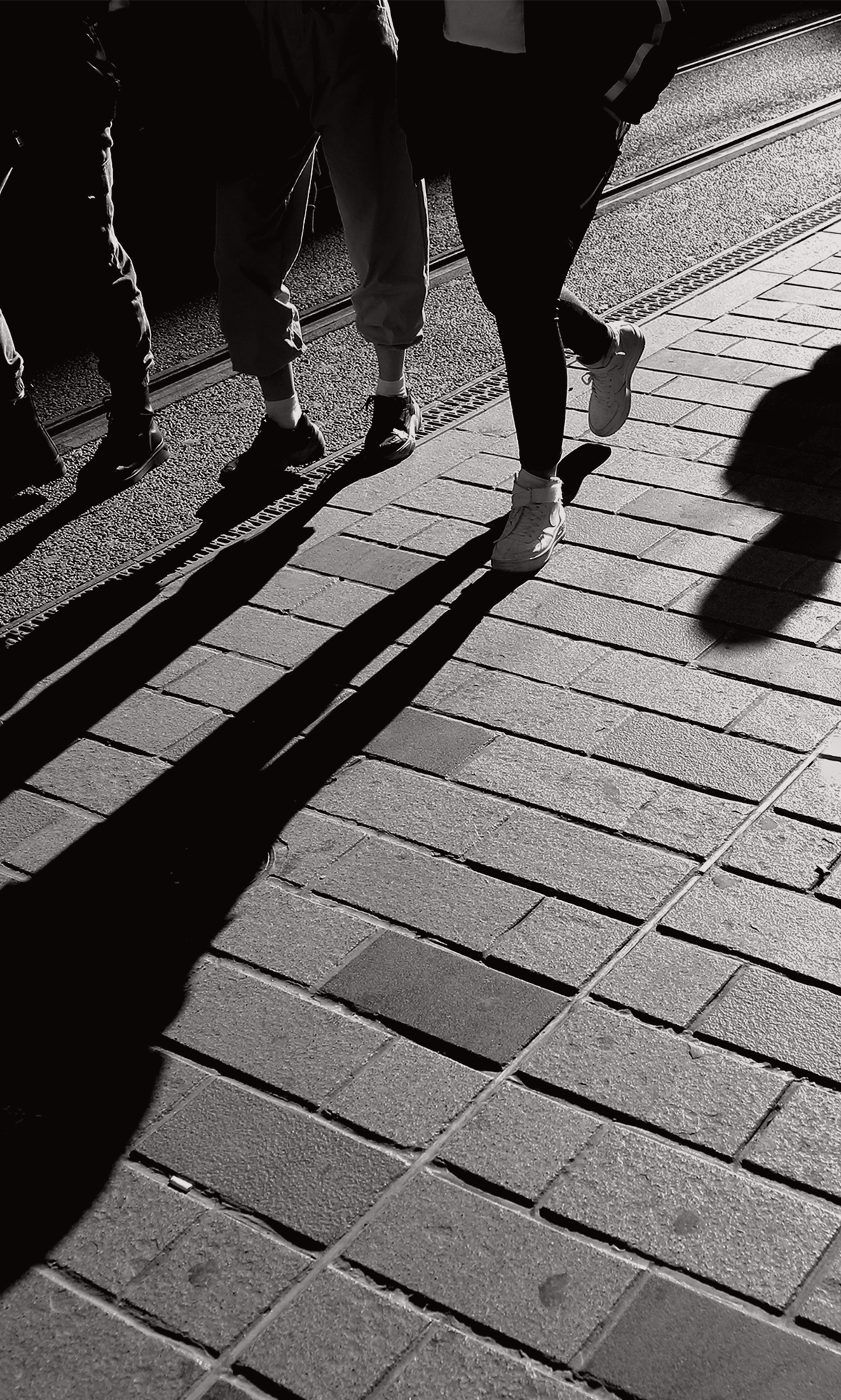 Walking feet and their shadows on a brick path